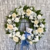 Heart-shaped floral wreath with cream roses, white flowers, and a blue ribbon on an easel