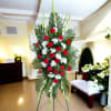 Standing floral spray with red and white carnations on a palm backdrop