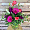 Pink roses and gerbera daisies in a glass vase with purple flowers