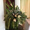 Tall arrangement of cream calla lilies and abundant cascading greenery in a clear glass vase