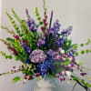 Tall arrangement of purple and blue hydrangeas, stock, orchids, and bells of Ireland in a white pedestal vase