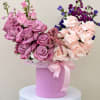 Pink and lavender roses arranged in a round hatbox with a ribbon