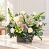 Mixed floral arrangement in a square gray vase with cream, pink, and green blooms