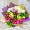 Hand-tied bouquet with pink roses, green hydrangeas, white chrysanthemums and red blooms in purple and gold wrap