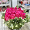 Round arrangement of hot pink roses with a ring of variegated leaves in a low glass vase