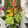 Tall tropical arrangement with red heliconia, yellow gerberas and green hydrangea in a square glass vase