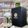 Single white rose under a glass dome with ribbon and black gift box on a wooden surface