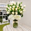 White roses and hydrangeas in a clear glass vase with a raffia bow