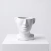 White face-shaped ceramic planter on a white pedestal