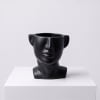 Black face-shaped vase on a white pedestal