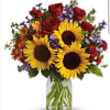 Bouquet of sunflowers, red roses, and purple flowers in a glass vase