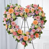 Heart-shaped floral wreath on a stand with pink, peach, and orange blooms