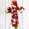 Floral cross arrangement with red roses, white carnations, and blue accents