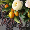 Arrangement with a white flower, orange citrus fruits, and dark berries in a dark vase