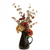Orange flowers in a dark ceramic pitcher vase with airy tan foliage