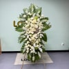 Tall standing floral spray with white roses and palm leaves on an easel
