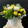 Yellow and white roses in a white vase with round silver-green foliage