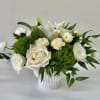 White roses and lilies arranged in a white vase with green filler