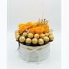 Orange roses in a round gift box with gold-wrapped chocolates and a crown topper