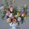 Pastel mixed flower arrangement in a white pedestal vase