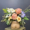 Peach roses and mixed flowers in a tan ceramic vase shaped like a torso