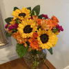 Bouquet of sunflowers, orange roses, and magenta flowers in a glass vase