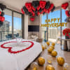 Anniversary room setup with heart balloons, rose petals, and a red rose bouquet