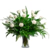 White roses arranged in a clear glass vase with lush greenery