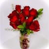 Red roses arranged in a clear glass vase with small greenery accents