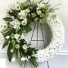 White floral wreath on a black stand with mixed blooms and greenery