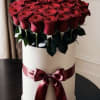 Red roses arranged in a white hat box with a burgundy ribbon