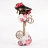 Graduation balloon display with a black cap balloon and pink and white balloons