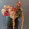 Tropical floral arrangement in a dark textured vase with burgundy orchids and anthurium
