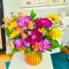 Bright mixed bouquet in a striped glass vase with pink, orange, and yellow blooms.