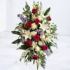 Tall standing spray of red and white roses, white lilies, and soft lavender blooms framed by ferns.