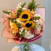 Bouquet of sunflowers, roses, and white blooms wrapped in pink paper