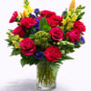 Mixed bouquet of red roses, carnations, and yellow snapdragons in a glass vase