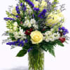 Mixed bouquet of yellow roses, white blooms, and purple flowers in a glass vase