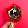 Hand holding a red sticker with a snarling raccoon and the words "the horror!"
