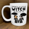 White mug with witch-themed text and two illustrated witches holding umbrellas