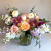 Mixed bouquet of roses, orchids, and white blooms in a glass vase