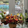 Autumn floral arrangement in a pumpkin-shaped vase with red, orange, and yellow blooms