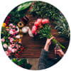 Hands trimming pink flowers beside ribbons and greenery on a wooden table