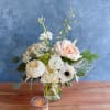 Cream and blush flowers arranged in a clear glass vase with a candle in front.