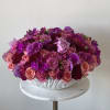 Round arrangement of pink and purple flowers in a white bowl vase