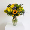 Yellow and purple mixed bouquet in a clear glass vase with a raffia bow