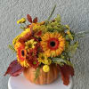 Autumn floral arrangement in a pumpkin-shaped container with orange and yellow blooms