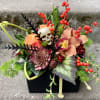 Halloween floral arrangement with a skull and orange orchids in a black container