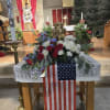Floral arrangement with red, white, and blue flowers on a table draped with an American flag.