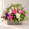 Mixed pink and purple flowers arranged in a wooden box with greenery